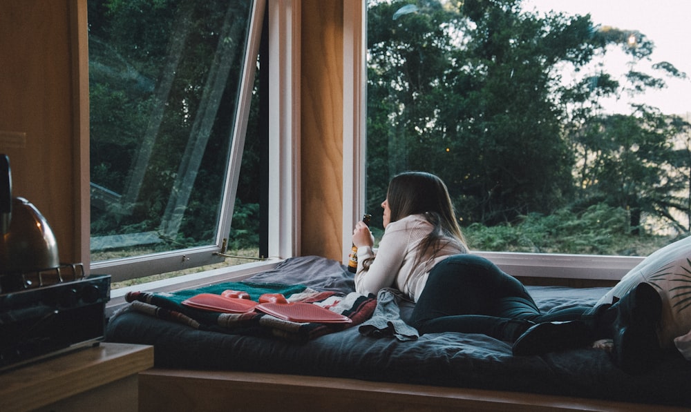 woman lying on bed next to glass window