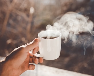 person holding white ceramic cup with hot coffee