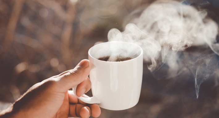 person holding white ceramic cup with hot coffee