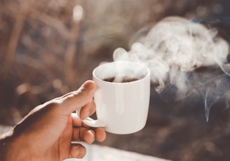 person holding white ceramic cup with hot coffee