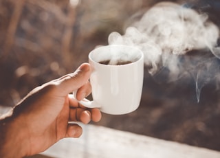 person holding white ceramic cup with hot coffee