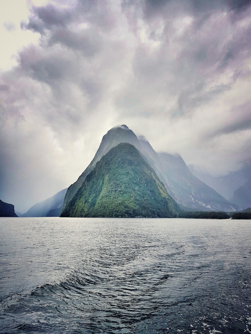 tree-covered mountain island under cloudy sky