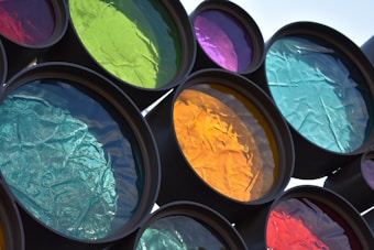A series of circular, colored translucent panels are arranged, each featuring different hues such as green, yellow, blue, and purple. The light filters through each one, creating vivid reflections. The textured surfaces give off a crinkled appearance, enhancing the visual interest.
