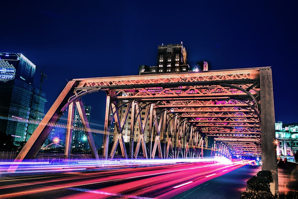 time lapse and light streaks photo of vehicle on bridge with high rise buildings in distant