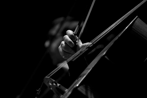 Close-up of hands playing a dark, resonant cello in a dimly lit room.