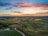 road between green grass field near mountains under blue and brown sky at golden hour