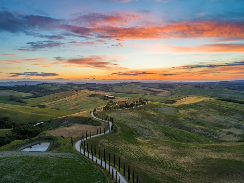 Strada tra il campo verde dell'erba vicino alle montagne sotto il cielo blu e marrone all'ora d'oro