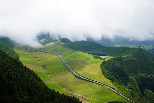 road between green grass field near mountains under white sky at daytime in Miradouro da Boca do Inferno Portugal