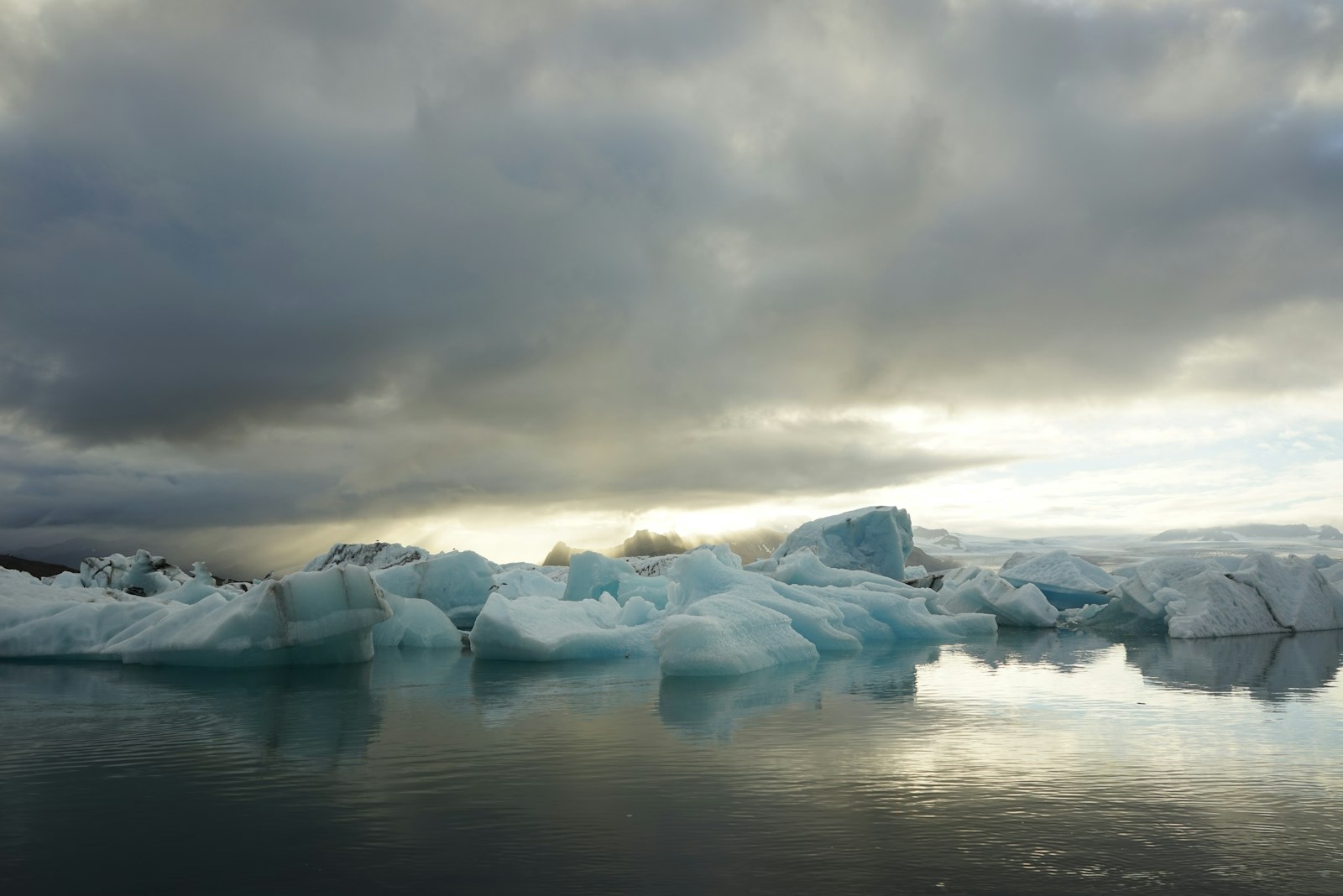Chunks of glacial ice floating on still water beneath a heavy grey sky