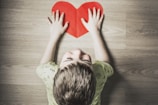 boy in green shirt holding red paper heart cutout on brown table