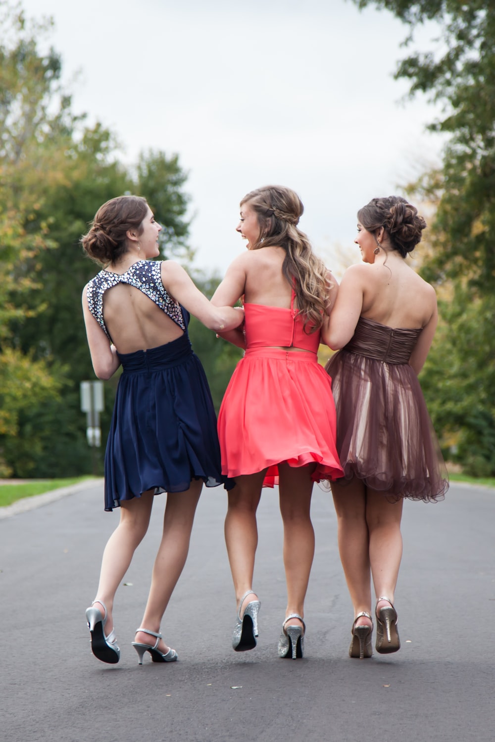 three women wearing red, brown, and blue dresses walking on concrete road during daytime