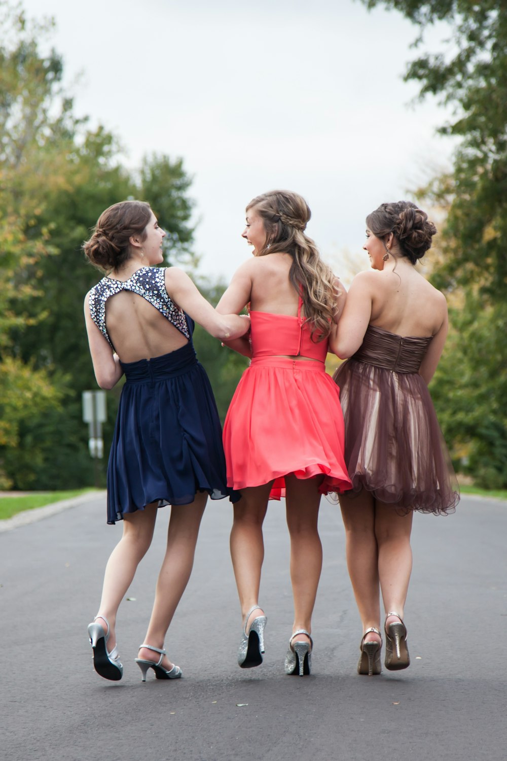 빨간색, 갈색, 파란색 드레스를 입은 세 명의 여성이 낮에 콘크리트 도로를 걷고 있습니다.