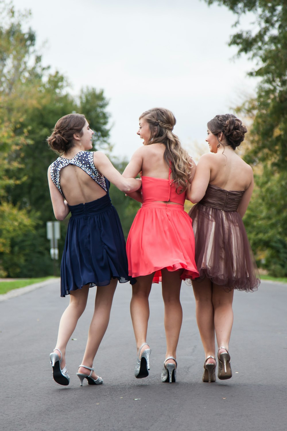 Trois femmes vêtues de robes rouges, brunes et bleues marchant sur une route en béton pendant la journée