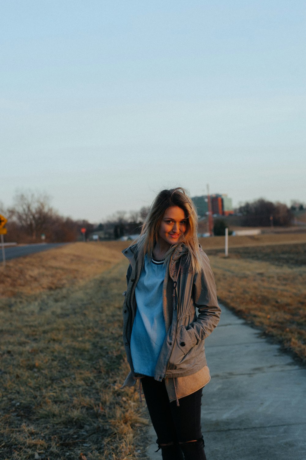 woman walking on sidewalk near grass field during daytime