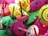 A collection of colorful wooden spinning tops with various vibrant patterns and concentric circles. The tops are primarily pink, green, yellow, and red with wooden handles, placed in a haphazard arrangement.