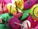 A collection of colorful wooden spinning tops with various vibrant patterns and concentric circles. The tops are primarily pink, green, yellow, and red with wooden handles, placed in a haphazard arrangement.