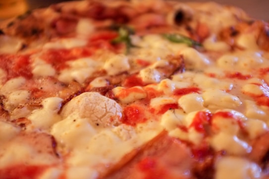 A close-up view of a pizza covered with melted cheese and a rich tomato sauce. Bits of fresh basil can be seen scattered across the surface, adding a touch of green. The crust appears to be baked to a golden-brown color, suggesting a crispy texture.