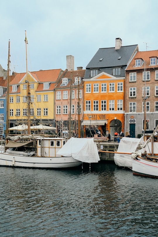 white wooden boats docks near assorted-color concrete houses during daytime in Nyhavn Denmark