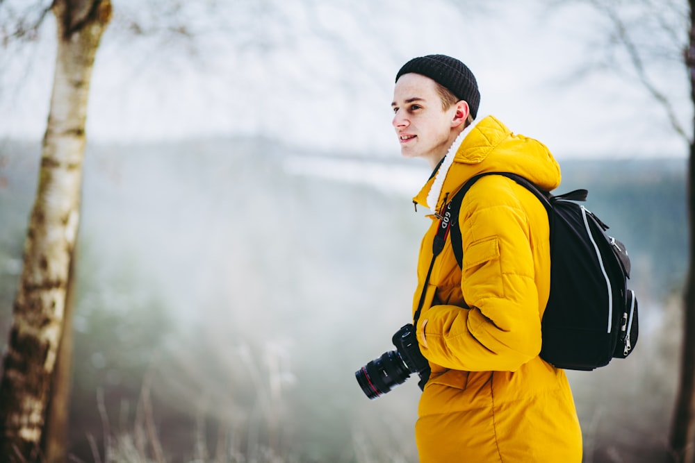 selective focus photography of man standing on cliff with DSLR camera hanging on neck