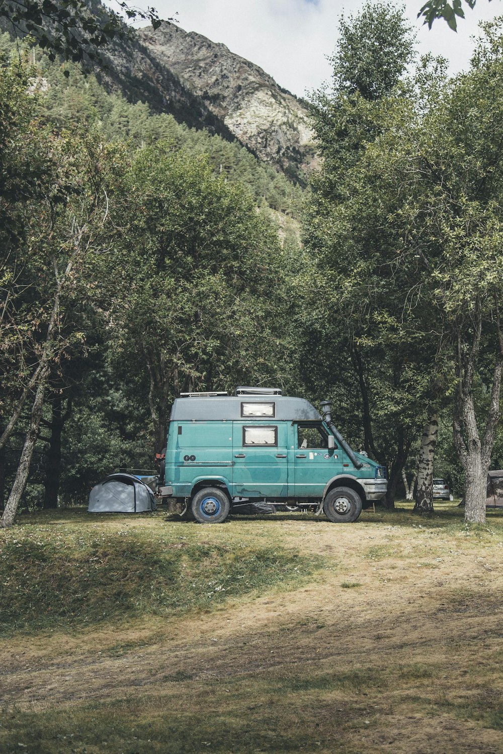 Landschaftsfotografie von geparktem blaugrünem und schwarzem Umbauwagen in der Nähe von Bäumen