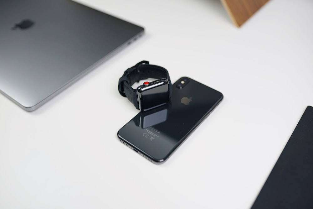 space gray aluminum case Apple Watch with black Sport Band on space gray iPhone X beside silver MacBook