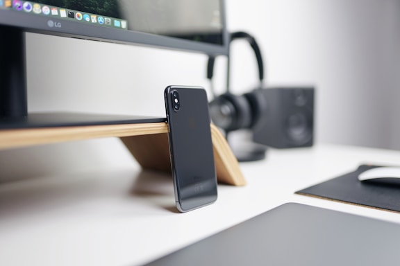 A modern workspace with a laptop, phone stand, and wireless speaker on a desk