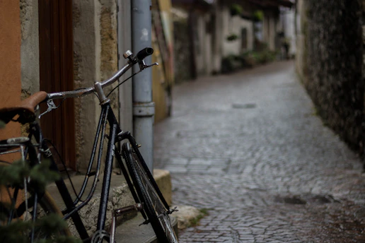 Desaturated, grainy photo of a gravel bike leaning against a rugged stone wall in a quiet Barcelona alley.