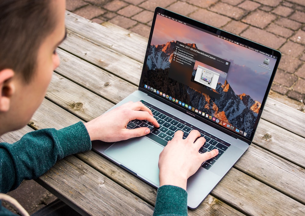 someone using a refurbished Apple Macbook outside on a picnic table.