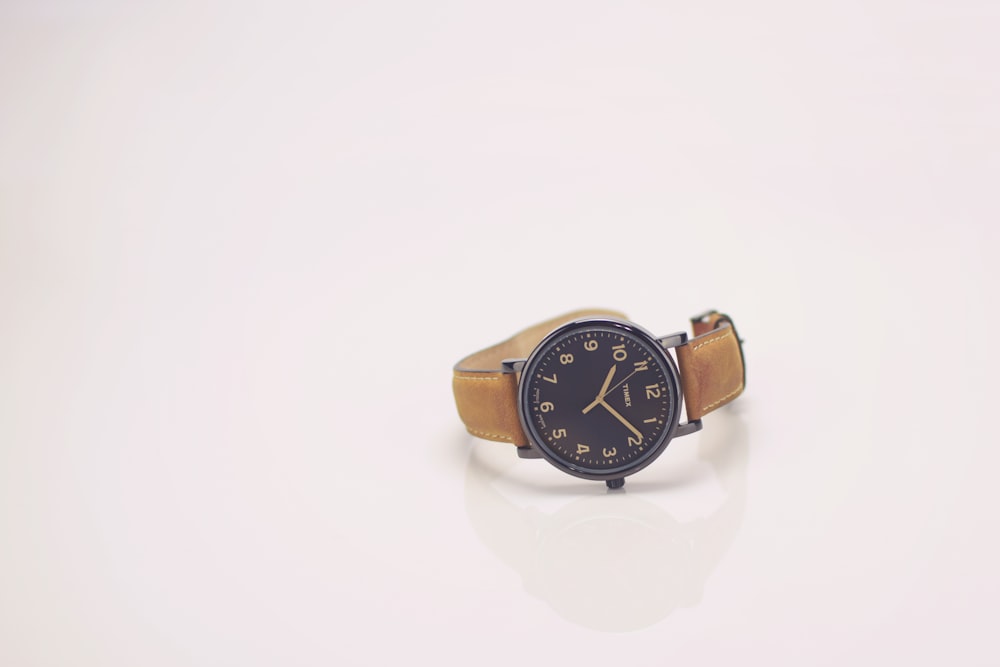 round black analog watch with brown leather band reading at 10:10