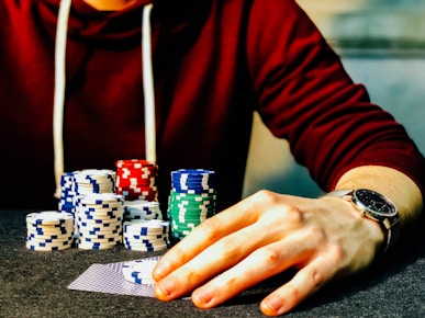 person holding playing cards beside poker chips