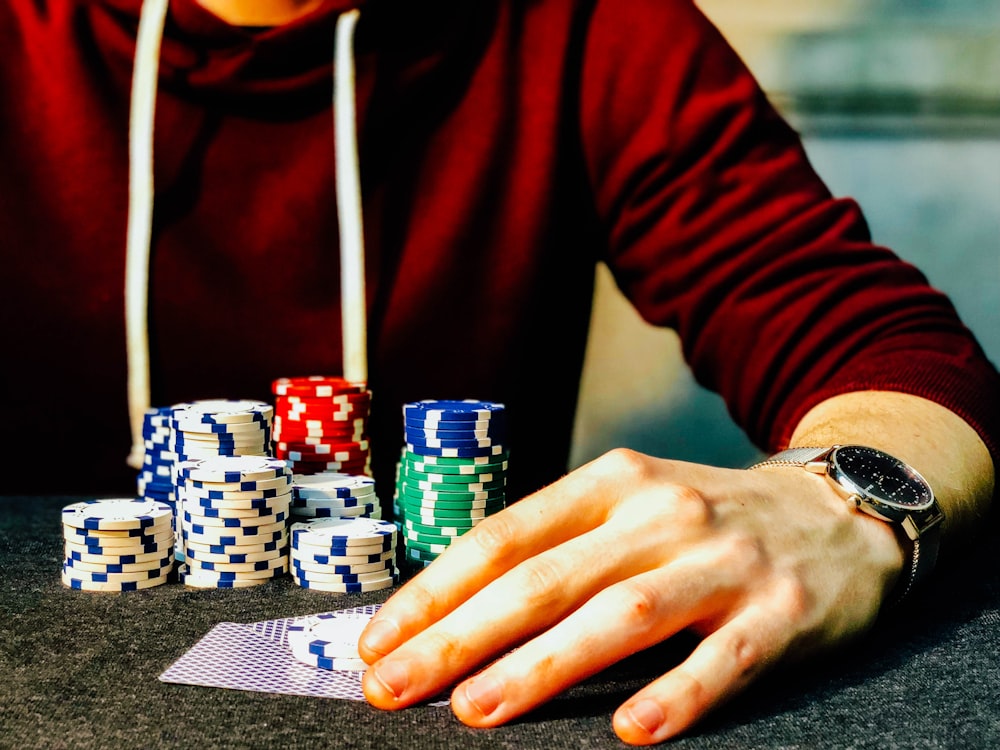 person holding playing cards beside poker chips