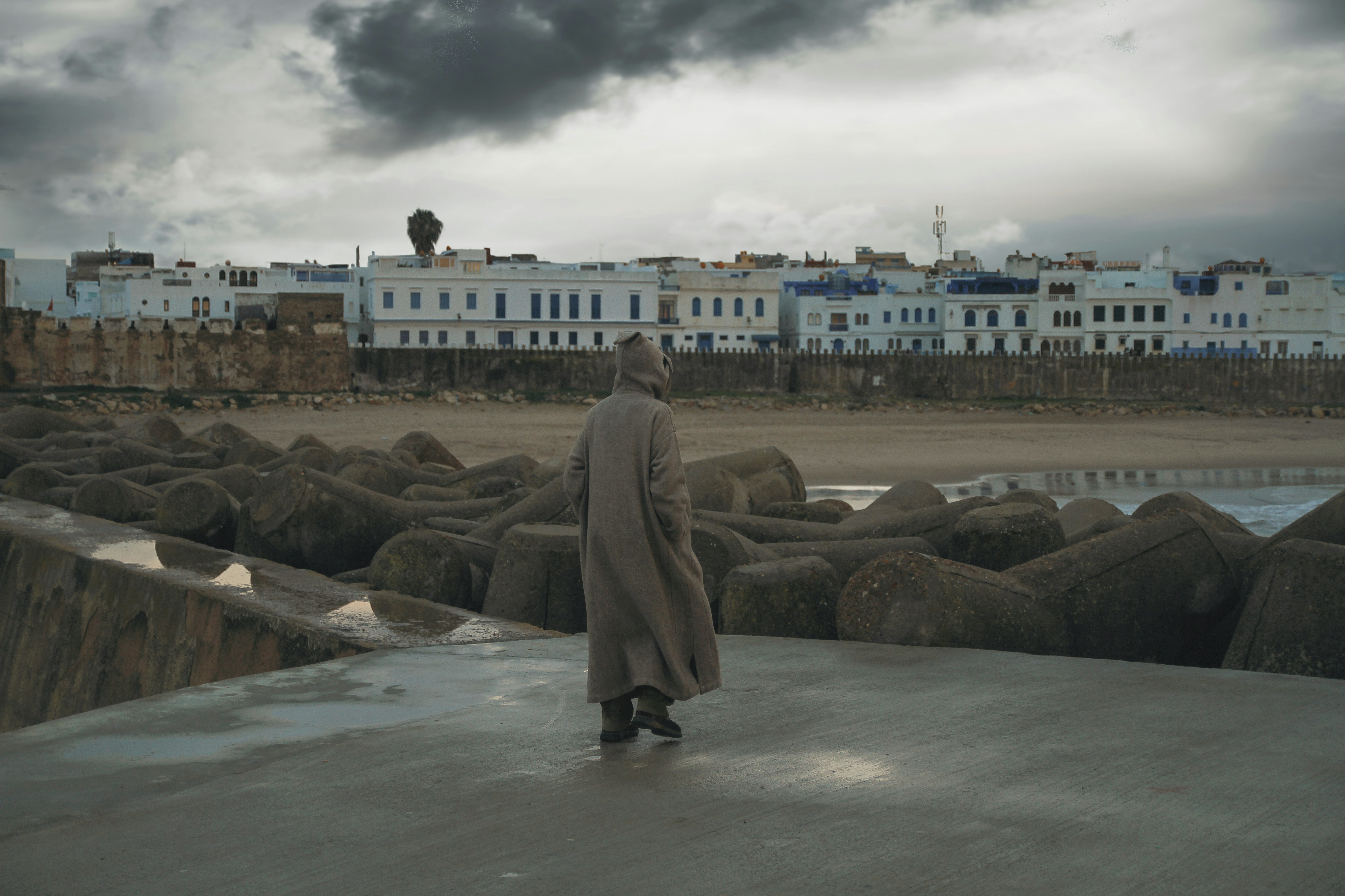 woman in brown coat standing on gray rock near body of water during daytime