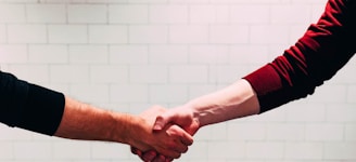 two person shaking hands near white painted wall