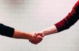 two person shaking hands near white painted wall