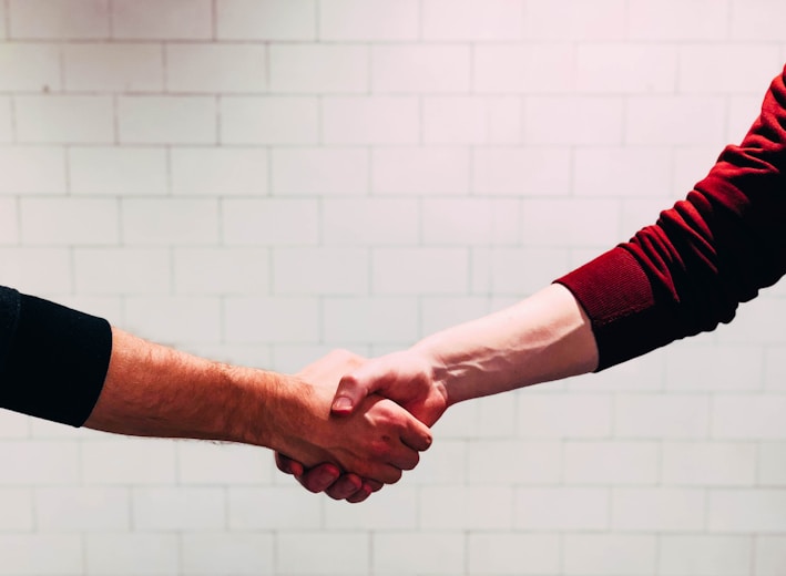 two person shaking hands near white painted wall