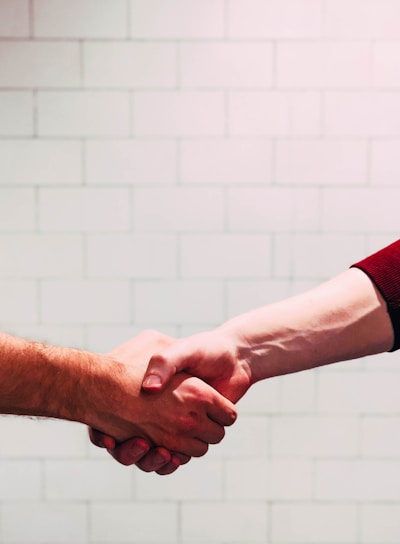 two person shaking hands near white painted wall