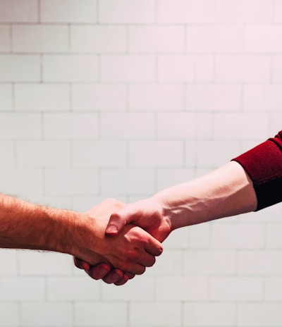 two person shaking hands near white painted wall