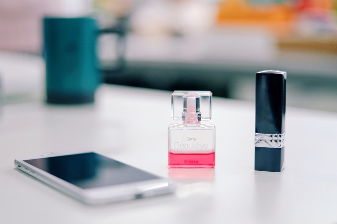 smartphone on a table next to fragrance bottle and black lipstick bottle \