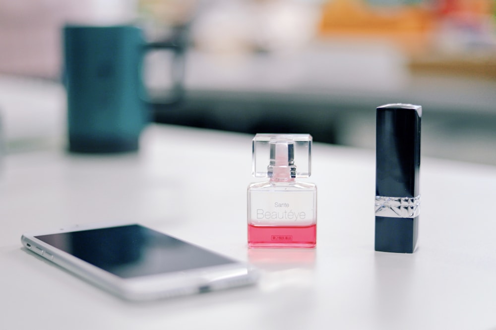 smartphone on a table next to fragrance bottle and black lipstick bottle \
