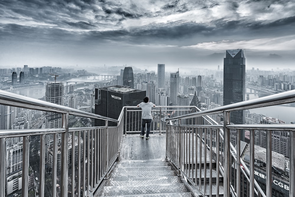man standing while hands resting on guard rail overlooking the city