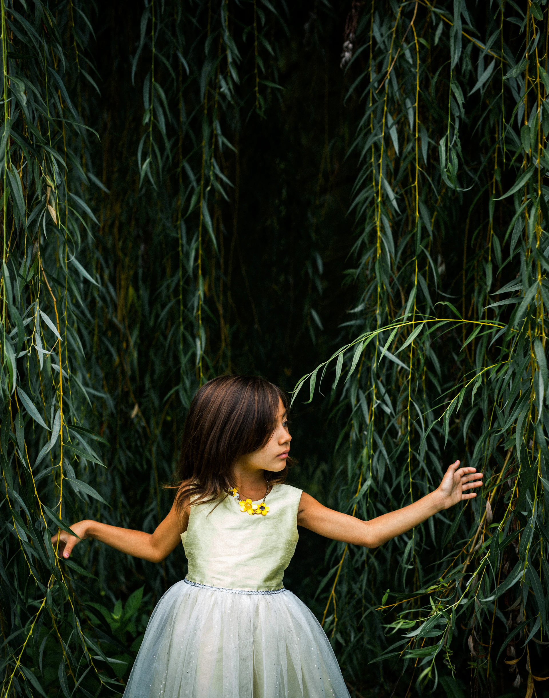 Rae, a wide-eyed 12-year-old girl, standing beside her mother near an ancient willow tree, its twisted branches whispering secrets in the wind.