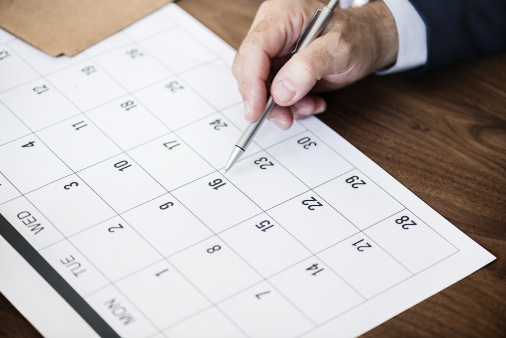 man holding pen pointing on calendar