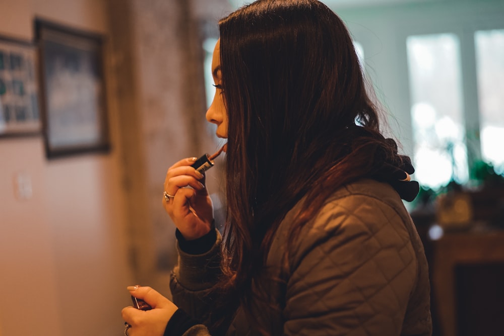 woman in brown quilted hoodie holding lipstick shallow focus photography