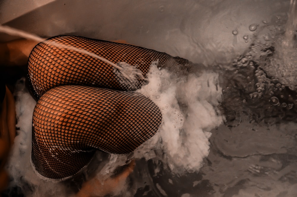 knee of woman wearing mesh stockings inside bathtub with water