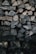 A stack of neatly arranged firewood featuring a variety of cut logs. The logs display different sizes and patterns of bark and wood grain, with most pieces split into manageable sections. The lighting is dim, highlighting the textures and natural tones of the wood.