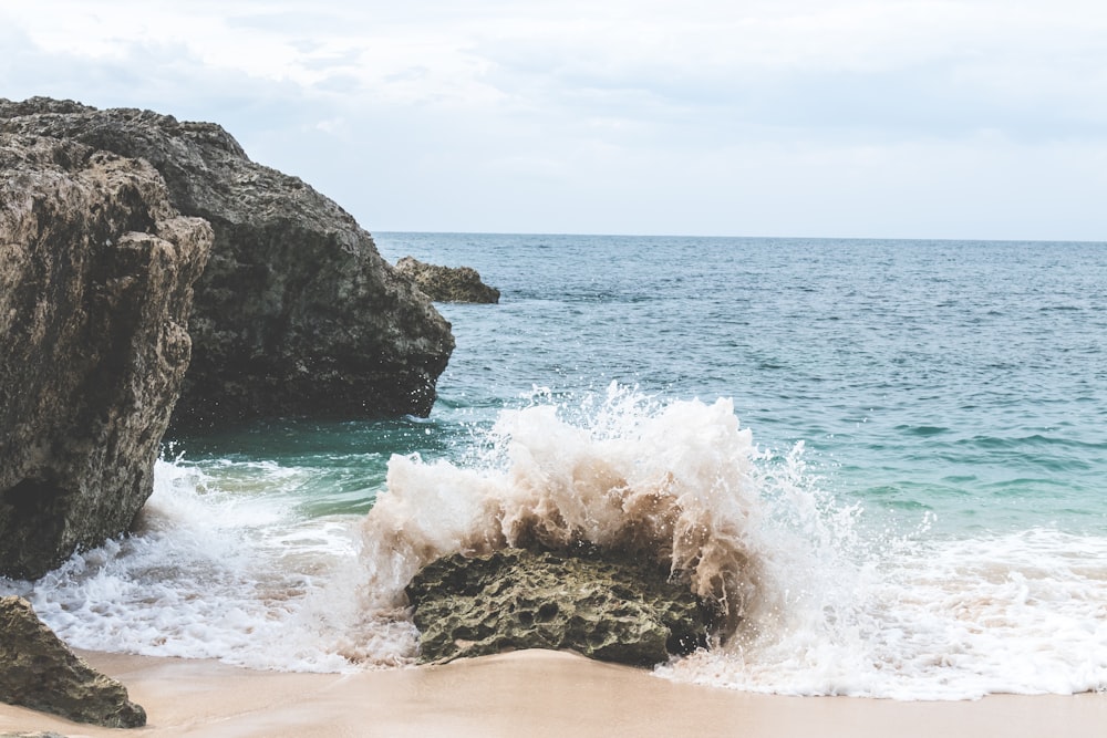 waves splashing on rock under white sky