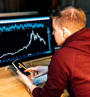 man holding black smartphone with flat screen monitor in front