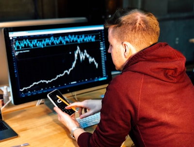 man holding black smartphone with flat screen monitor in front