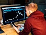 man holding black smartphone with flat screen monitor in front