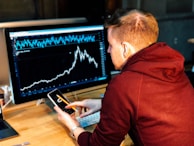 man holding black smartphone with flat screen monitor in front